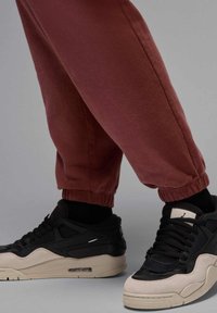 Bordeauxfarbene Jogginghosen mit elastischen Bündchen, kombiniert mit schwarz-weißen Sneakers, die eine Mischung aus Texturen aufweisen und eine sichtbare Luftpolsterung in der Sohle haben.