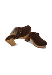 Sabots en daim marron avec talons épais en bois et brides latérales réglables à boucle, avec une couture blanche le long des bords supérieurs.