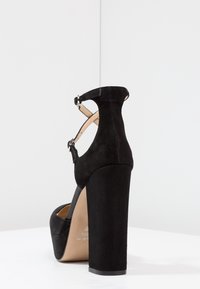 Černá semišová vysoká bota na podpatku s páskem kolem kotníku, čtveratou špičkou a masivním podpatkem, se hladkým vnitřním podšívkou a dvěma nastavovacími přezkami.