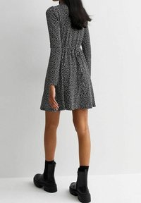 Svart klänning med vita prickar, långa ärmar, elastisk midja, utsvängd kjol. Parat med svarta ankelstövlar. Slät tygtextur.