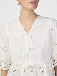 Vestito bianco con maniche a sbuffo, caratterizzato da ricami ad occhiello e una scollatura a V con lacci sul davanti. Tessuto di cotone morbido, vita arricciata.