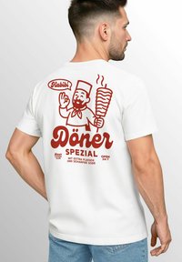 Weißes T-Shirt mit einem roten Grafikmotiv eines lächelnden Kochs mit einem Döner, Text "Döner Spezial" und "24/7 geöffnet" in stilisierten Schriftarten.