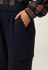 Pantalones azul marino con un bolsillo con detalle de solapa, combinados con una camisa de cuadros marrón de manga larga. Tejido suave con cintura elástica.