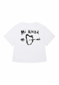 Witte oversized t-shirt met de tekst "Mi Amor" en een hart doorboord door een pijl in zwarte opdruk op de achterkant.