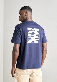 Námořnické tričko vyrobené z bavlny, s velkým bílým grafickým designem na zadní straně. Krátké rukávy, volný střih a standardní kulatý výstřih.