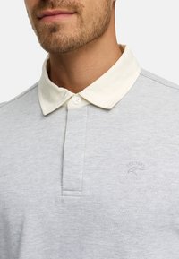 Lys grå polo t-shirt med en kontrasterende hvid krave, har en to-knaps placket og broderet logo på venstre bryst. Blødt bomuldsstof.