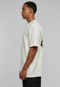 Bomull T-skjorte i off-white med løs passform, korte ermer og et grønt grafisk design på baksiden, med en glatt tekstur.