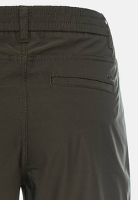 Dunkelgrüne, dehnbare Hosen mit einem elastischen Bund, die eine Gesäßtasche mit einer schmalen Öffnung und minimalen Nähdetails aufweisen.