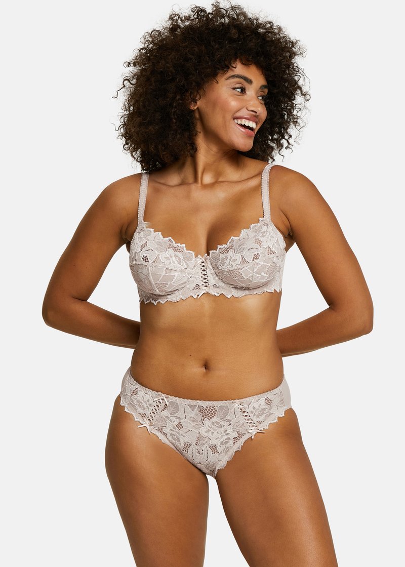 Lace beha en slip set in lichtbeige, met bloemige patronen, golvende randen en verstelbare bandjes. Zachte textuur met ingewikkelde details.