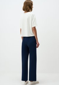 Witte cropped t-shirt met korte mouwen, gecombineerd met marineblauwe wijde broek, met een gladde textuur en een minimalistisch ontwerp.