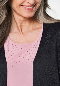 Schwarze Strickjacke mit strukturiertem Design, kombiniert mit einem pinken Oberteil, das mit Strasssteinen verziert ist, wodurch ein schichtiger Look entsteht.