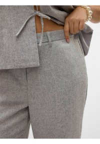 Grijze textuuroutfit met een aansluitend top met een gestrikt detail en bijpassende broek. Close-up van de zijzak en het stofpatroon.