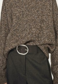 Hnědý pletený svetr s texturovaným povrchem, spárovaný s tmavými kalhotami a silným černým pásem s kulatou stříbrnou sponou.