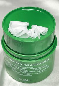 Zielony słoik z balsamem oczyszczającym z zakręcaną pokrywką, wypełniony białym, miękkim, złożonym produktem. Składniki wyraźnie wydrukowane po bokach.