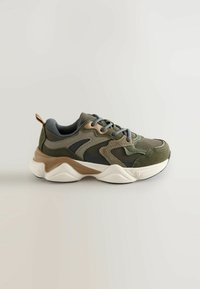 Žalios ir pilkos sportinės sneakers su tinklinės medžiagos, tekstūrinio zomšinės akcentais, masyviu baltu padu ir kontrastingomis smėlinėmis detalėmis.