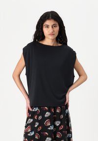 Top scurt negru cu mâneci scurte și croială relaxată, cu un decolteu larg. Asortat cu o fustă cu un model care prezintă desene colorate de scoici pe un fundal negru.