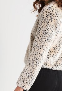 Cremefarbene Fake-Fur-Jacke mit einem schwarzen Leopardenmuster. Sie verfügt über lange Ärmel und eine lockere Passform und zeigt eine weiche, strukturierte Oberfläche.