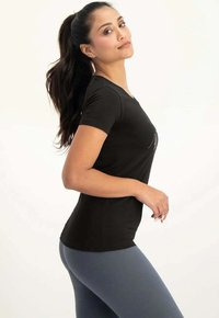 Svart kortärmad åtsmitande topp med rund halsringning, matchad med högmidjade blå leggings. Slät tyg med en liten glans.