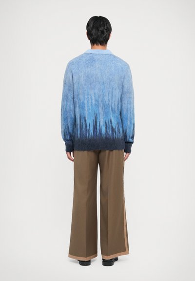 Maglione a maglia con gradiente blu e grigio, dalla vestibilità ampia e maniche lunghe, abbinato a pantaloni larghi marroni con dettagli laterali.