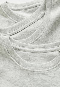Trois T-shirts gris empilés, dotés d'encolures ras du cou, de bords côtelés et d'une texture douce et chinée. Tissu en coton avec une finition lisse.