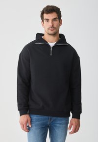 Sweatshirt preto de pulôver com gola alta, meio zíper e detalhes em ribana. Tecido macio com um corte relaxado e mangas longas.