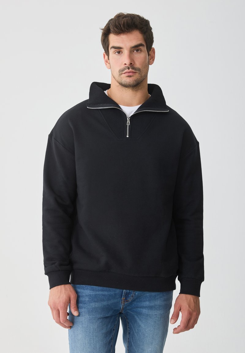 Sweatshirt preto de pulôver com gola alta, meio zíper e detalhes em ribana. Tecido macio com um corte relaxado e mangas longas.