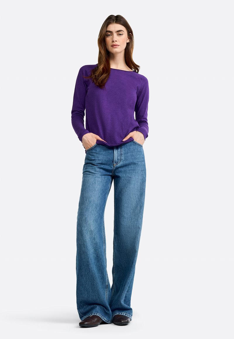 Purple long-sleeve top paired with wide-leg blue denim jeans. The jeans feature a classic five-pocket design and textured fabric.