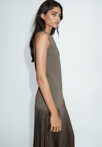 Olivgrünes ärmelloses Oberteil aus glattem Stoff, kombiniert mit einem plissierten, bodenlangen Rock in einem sanften Braunton, minimalistisches Design.