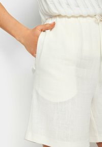 Witte linnen shorts met een elastische tailleband, zijzakken en een relaxte pasvorm. Lichte textuur met subtiele, geweven patronen.