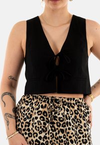 Top corto negro con escote en V y detalle de lazo en el frente, combinado con pantalones beiges con estampado de leopardo negro. Textura suave y diseño ajustado.