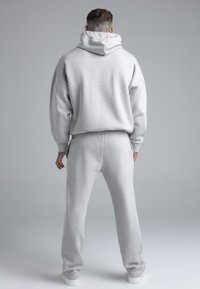 Grijze fleece hoodie en bijpassende joggers met een relaxte pasvorm. De stof lijkt zacht met een gladde textuur. Er worden witte sneakers gedragen.