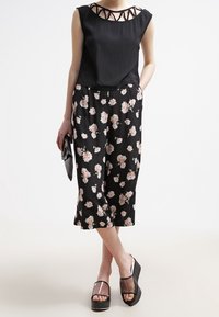 Pantalones culottes de estampado floral negro con una blusa negra sólida que presenta un diseño con corte en el escote, combinados con sandalias de plataforma con tiras transparentes.