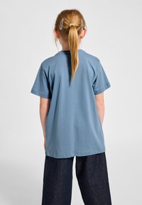 Bomullst-shirt i mjuk blå färg, kortärmad, med ledig passform. Kombinerad med mörka jeansbyxor, visar en enkel design utan logotyper eller mönster.