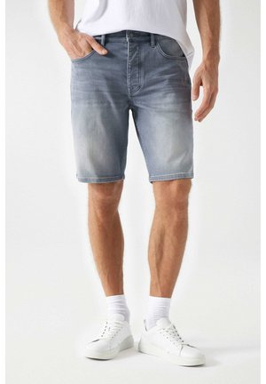 Jeans-Shorts in Hellblau mit klassischem Fünf-Taschen-Design, dezentem Ausbleichen und geradem Schnitt, kombiniert mit weißen Turnschuhen und Socken.