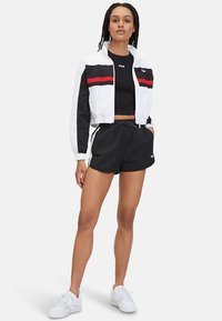 Przycięta biała i czarna kurtka z czerwonymi paskami, czarny krótki top, czarne szorty i białe trampki. Lekki, sportowy styl i casualowy krój.