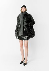 Chaqueta de cuero negra de gran tamaño sobre una falda corta negra con detalles plateados, combinada con una bufanda y guantes grises, finalizando con tacones negros.