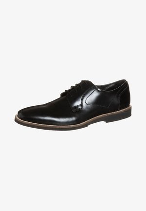 Chaussure habillée pour homme en cuir noir poli avec lacets avant et semelle basse bordée de beige, inclinée pour montrer le côté extérieur et l'avant du pied.