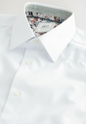 Balta pogu krekls, izgatavots no teksturēta auduma, ar ziedu raksta iekšējo apkakli un etiķeti ar "NEXT TAILORING" dizainu.