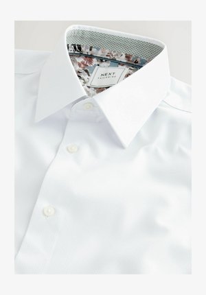 White button-up shirt made of textured fabric, featuring a floral patterned inner collar and a label with "NEXT TAILORING" design.