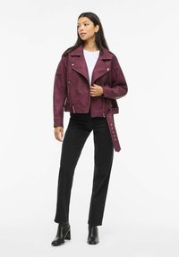 Burgundi värvi kunstnahast mootorrattajakk hõbedaste detailide, tõmblukuga taskute ja reguleeritava vööga. Sobitatud mustade teksade ja pahkluu saapadega.