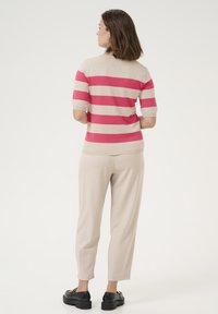 Gebreid T-shirt met korte mouwen, met afwisselend roze en beige strepen. Gepaard met lichtbeige broeken en zwarte schoenen.