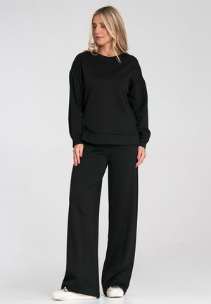 Czarny sweatshirt i szerokie spodnie z miękkiego materiału, z luźnym krojem i okrągłym dekoltem, w połączeniu z białymi sneakersami.
