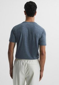 Tricou cu mânecă scurtă și guler rotund, dintr-un material gri chiné, asociat cu pantaloni cu talie elastică de culoare deschisă. Design minimalist.