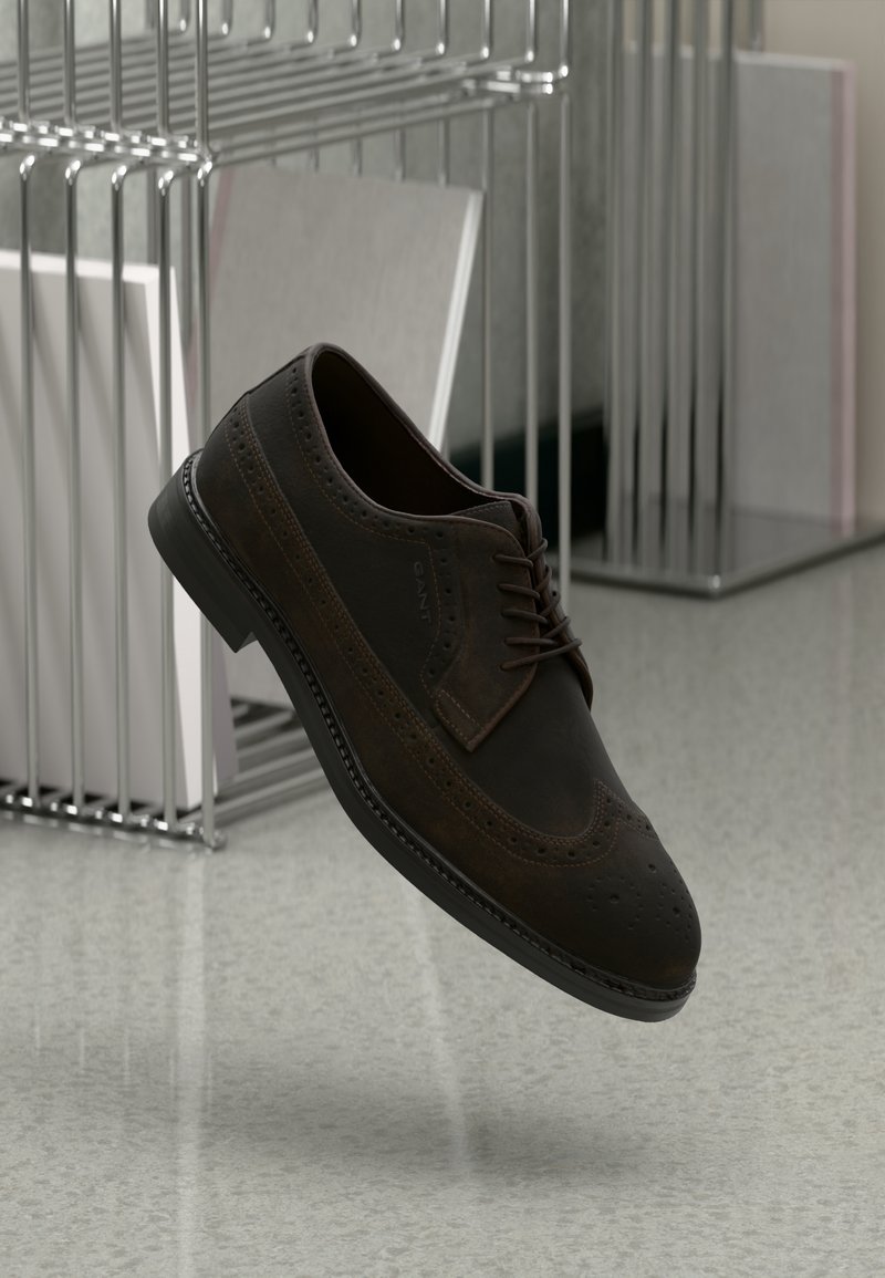 Zapato brogue de cuero marrón con detalles perforados, cordones y suela de goma plana. Exhibido en el aire contra un fondo moderno.