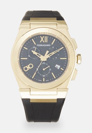 Montre en acier inoxydable doré avec bracelet en caoutchouc noir ; présente un cadran noir, un chronographe, une fenêtre de date et de grands chiffres romains.