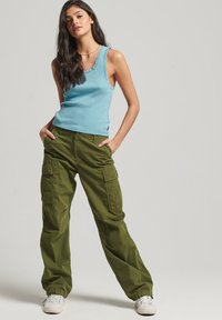 Top sin mangas azul claro con borde festoneado, combinado con pantalones cargo verde oliva que cuentan con múltiples bolsillos y un corte relajado. Zapatillas blancas.