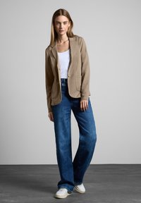 Beige liinapüksi, millel on nurgalapid ja kaks eesmist taskut, on kokku pandud laiade jalgevahedega siniste denimipükstega ning valgete sneakeritega.