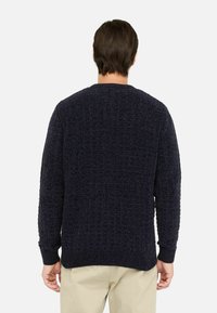 Maglione blu navy lavorato a maglia con un motivo testurizzato, scollo a girocollo e polsini a costine. Indossato con pantaloni chiari, visto da dietro.