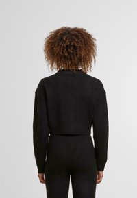 Fekete, rövidített, hosszú ujjú pulóver puha anyagból. Bordás szegéllyel és egyszerű, letisztult dizájnnal rendelkezik.