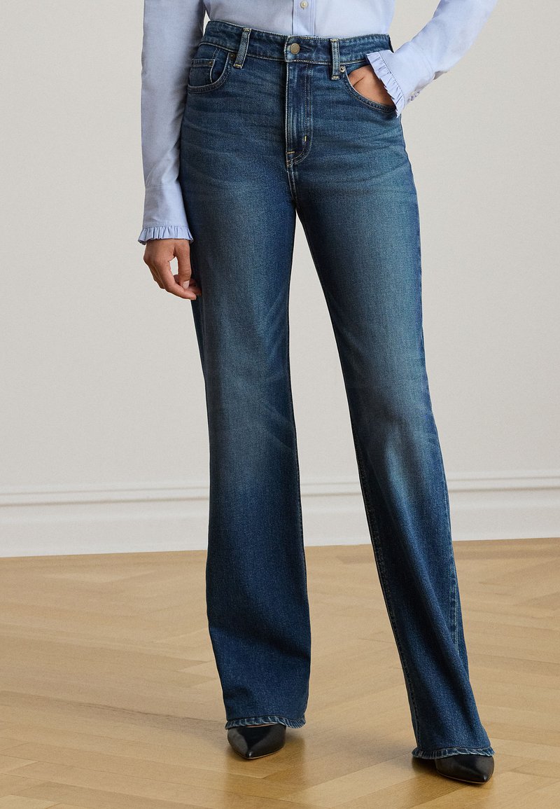 Μπλε τζιν παντελόνι με φαρδιά μπατζάκια και ψηλή μέση, με εμπρόσθιες τσέπες και διακριτική ξεθώριαση. Συνδυασμένο με μαύρα παπούτσια με μυτερή μύτη και ανοιχτόχρωμο πουκάμισο.